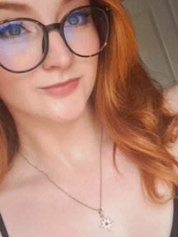 A woman with red hair and glasses smiles into the camera