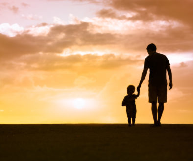 Father and son holding hands with a sunset in the background