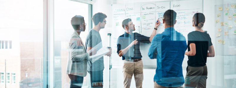 People having a standing meeting in a glass room.