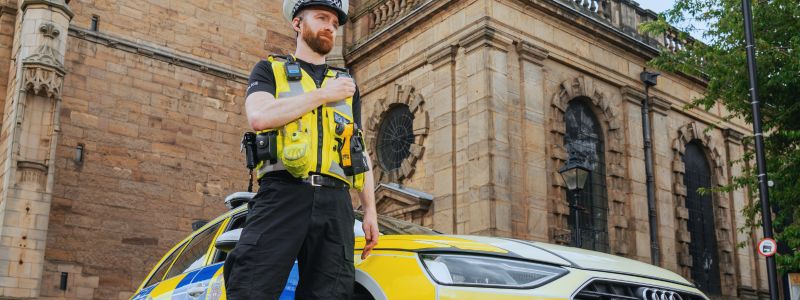 Our members_image Officer standing next to his car and holding his radio